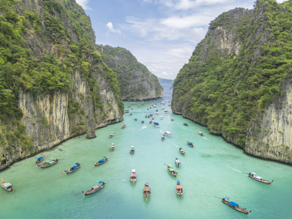 Aerial view of Phi Phi islands Travel Landmark of Krabi Phuket, Thailand. Drone POV fly over Pileh Lagoon with traditional long-tail boats floating on stunning turquoise waters. Maya beach natural popular destination for tourists in summer holidays.